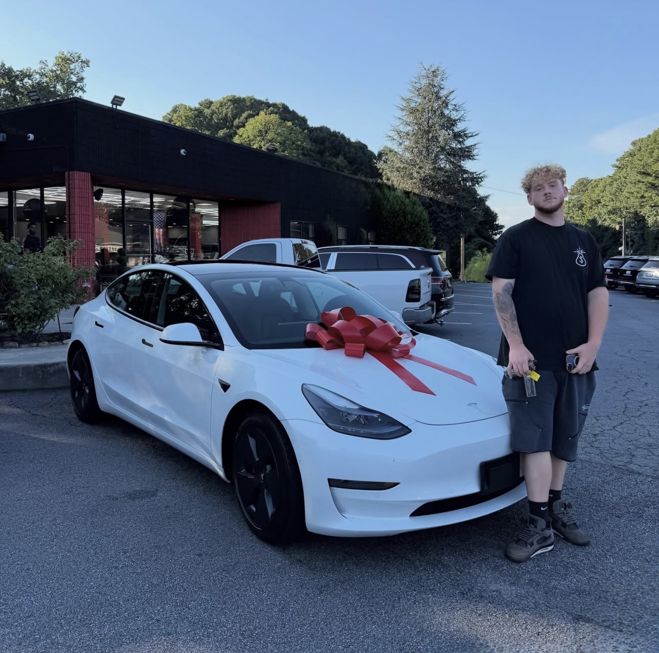 Customer next to his new white Tesla Model 3 with a red bow